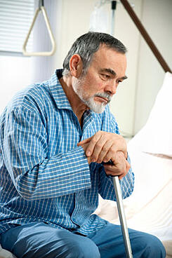 Elderly man with a cane on a hospital bed