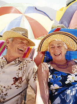 Smiling senior couple under a beach umbrella enjoying life after retirement