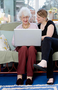 Young woman showing her grandmother how to use a laptop
