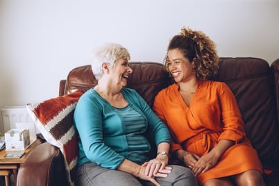 Senior woman laughing on a couch having a conversation with a young woman